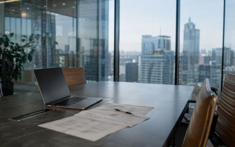 Glass-walled meeting room in a commercial tower with a laptop and printed evaluation sheets